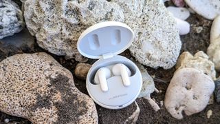 Hero image for best fake AirPods showing LG Tone Free T90 in white charging case paced on rocks 