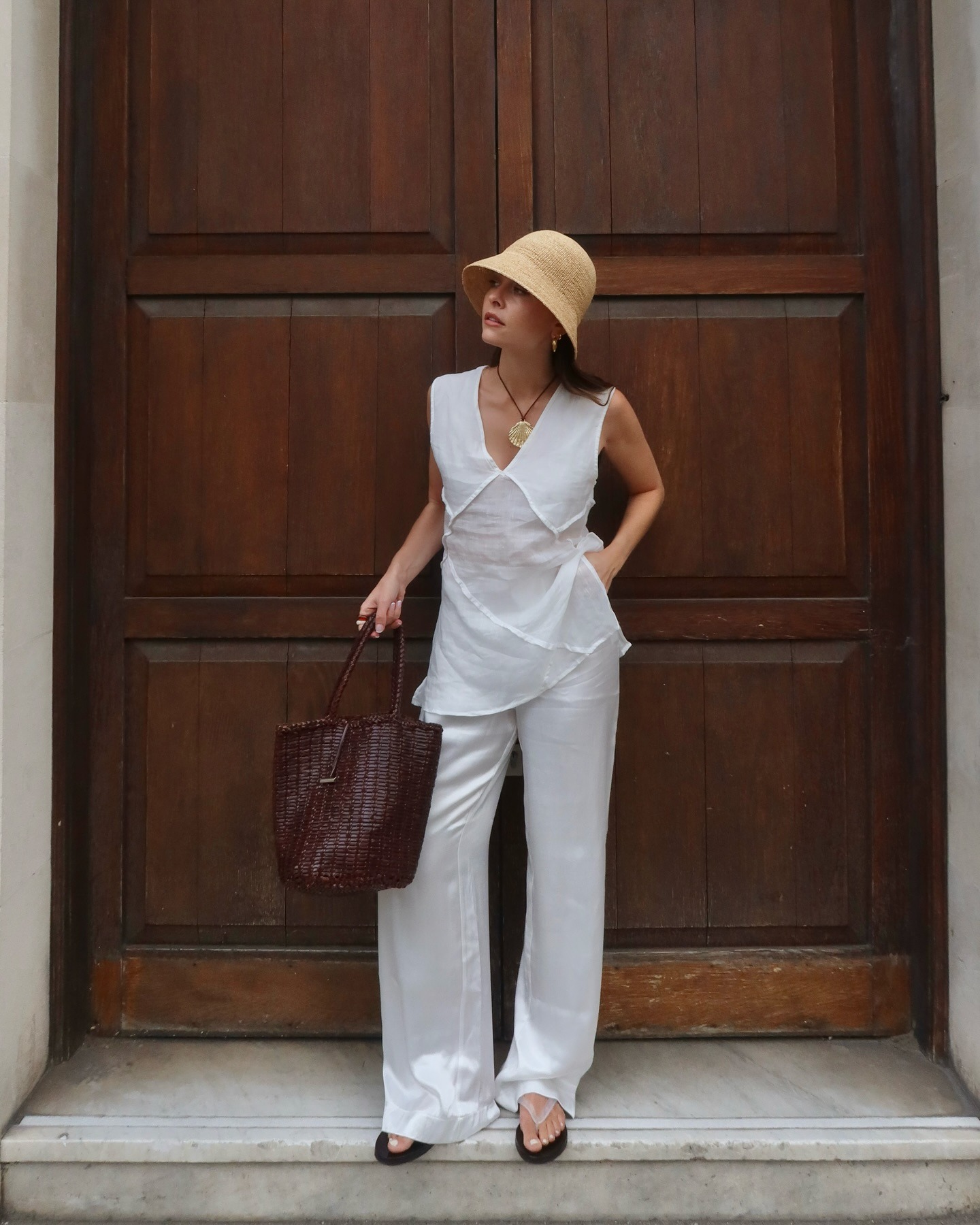 Woman wears crochet hat, linen top, white satin trousers, flip flops