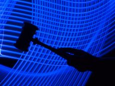 A photo of a silhouette of a hand holding a gavel is in the foreground, with a futuristic mesh of blue lines in the background