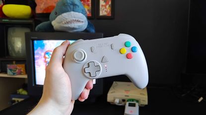 Hand holding Retro Fighters StrikerDC wireless controller in front of Sega Dreamcast connected to a Sony Trinitron CRT TV.