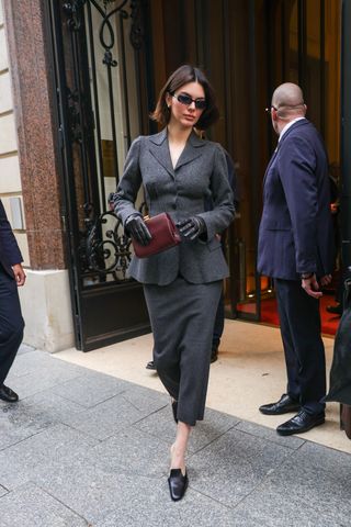 Kendall Jenner wearing a gray skirt suit with leather gloves and a burgundy clutch in Paris.