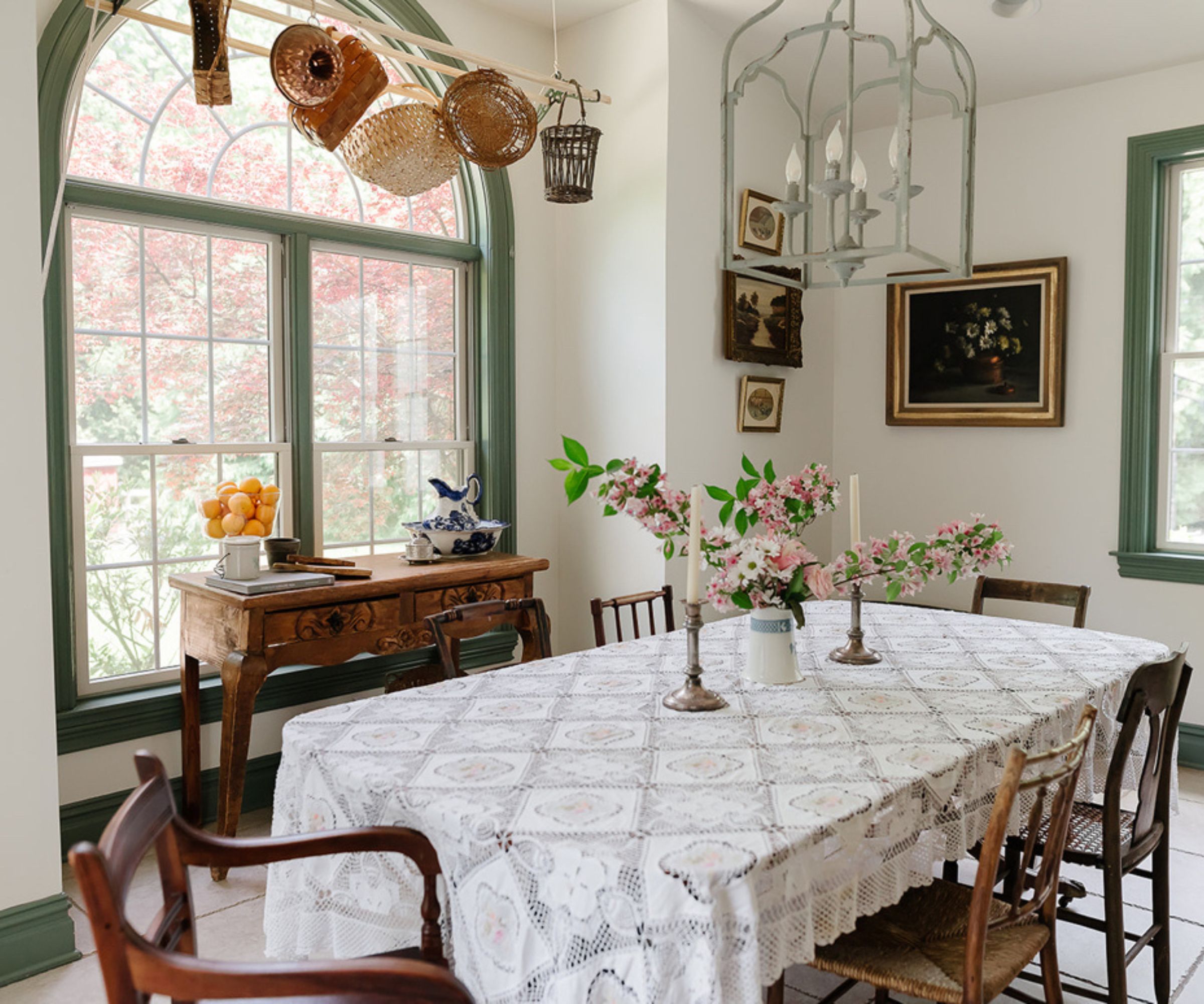 Vintage dining room with arched window, baskets hanging on ceiling, vintage table with tablecloth, wood chairs and candles