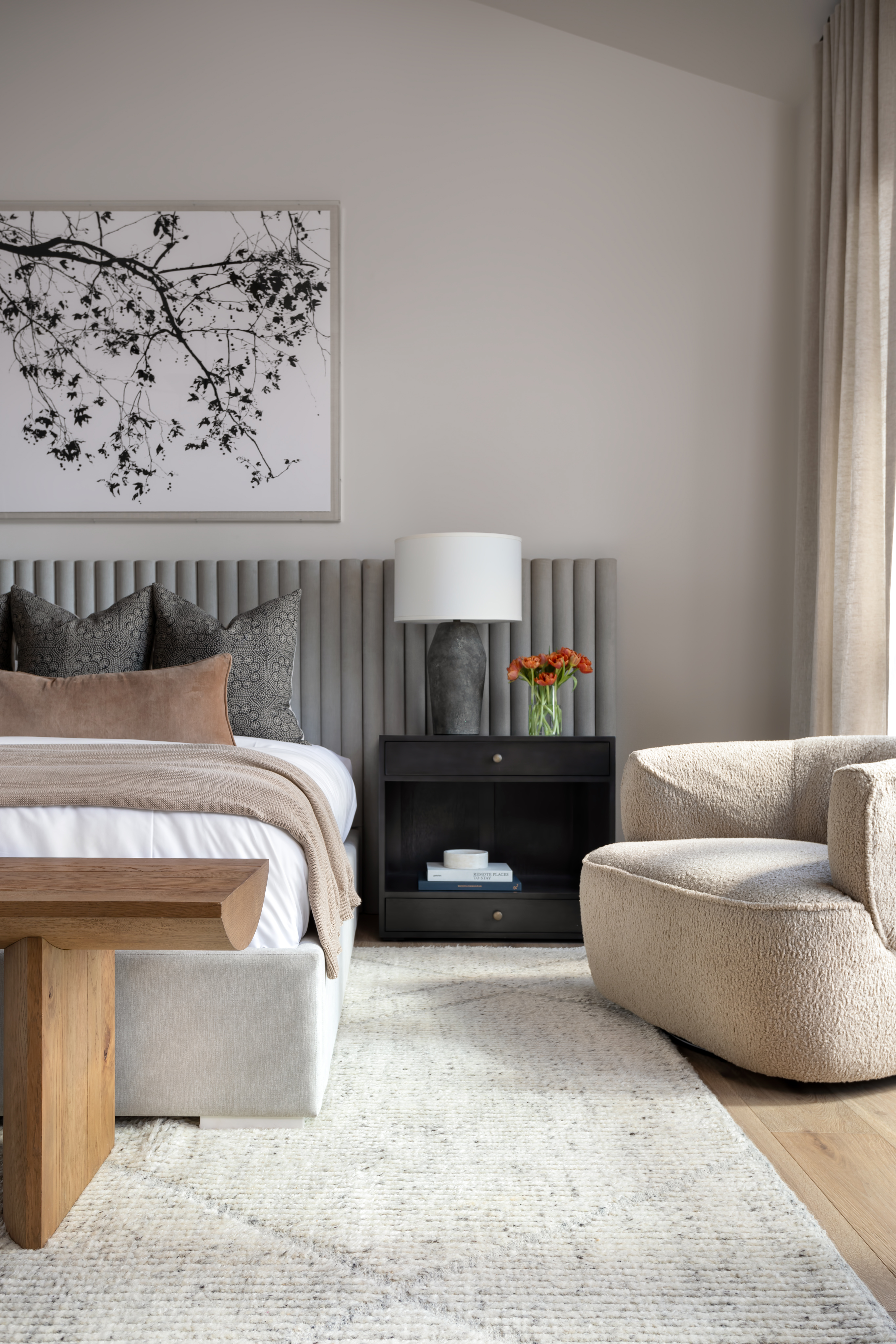 A bedroom with biege sofa and curtains and gray headboard and bedding