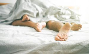 Two pairs of feet at bottom of bed