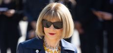 Anna Wintour wearing a navy trench coat and yellow necklace