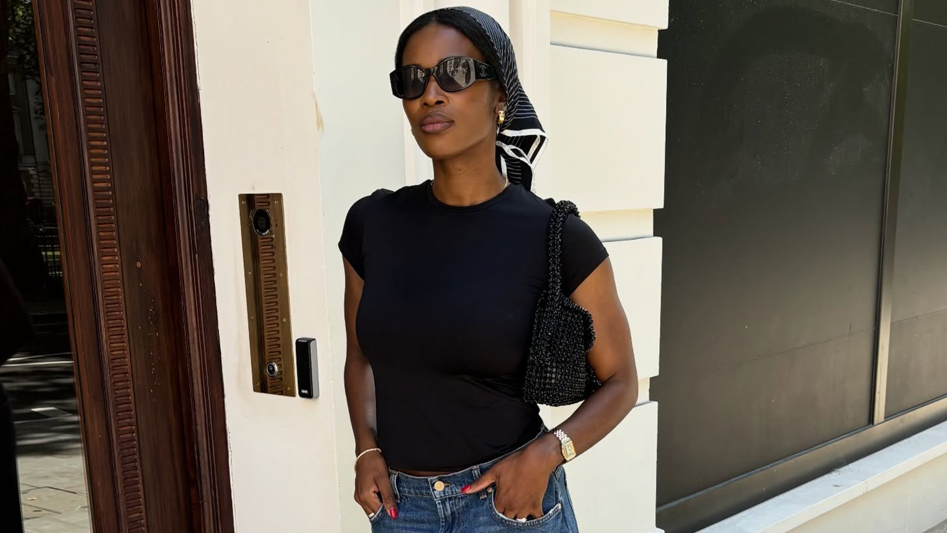 Woman wearing black t-shirt, black sunglasses, silk scarf, and mid-wash barrel leg jeans.