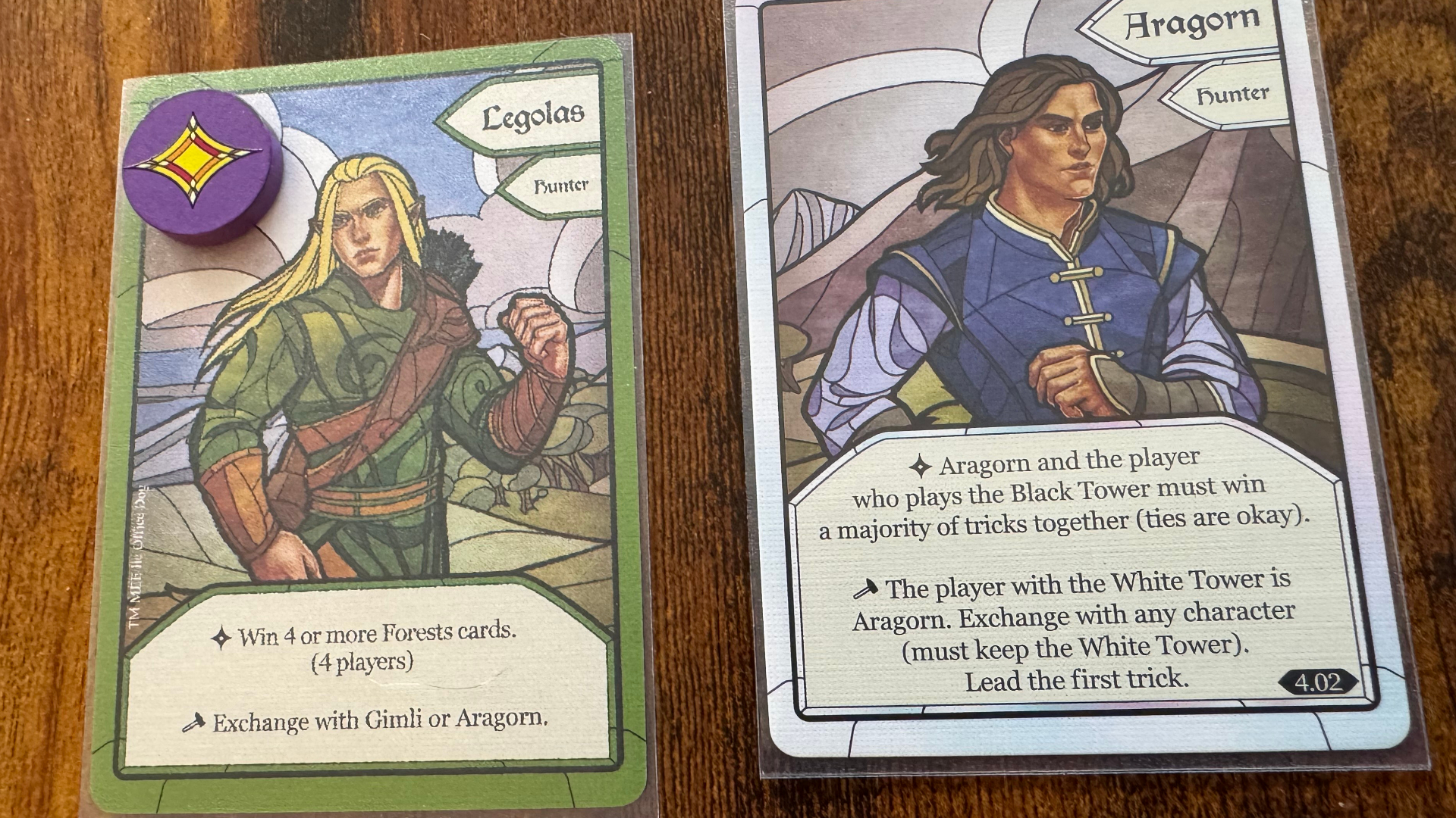 Two cards and a token from The Two Towers Trick-Taking Game, lying on a wooden surface