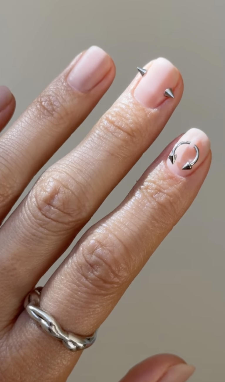 Short pale pink nails with small silver hoops through the tips
