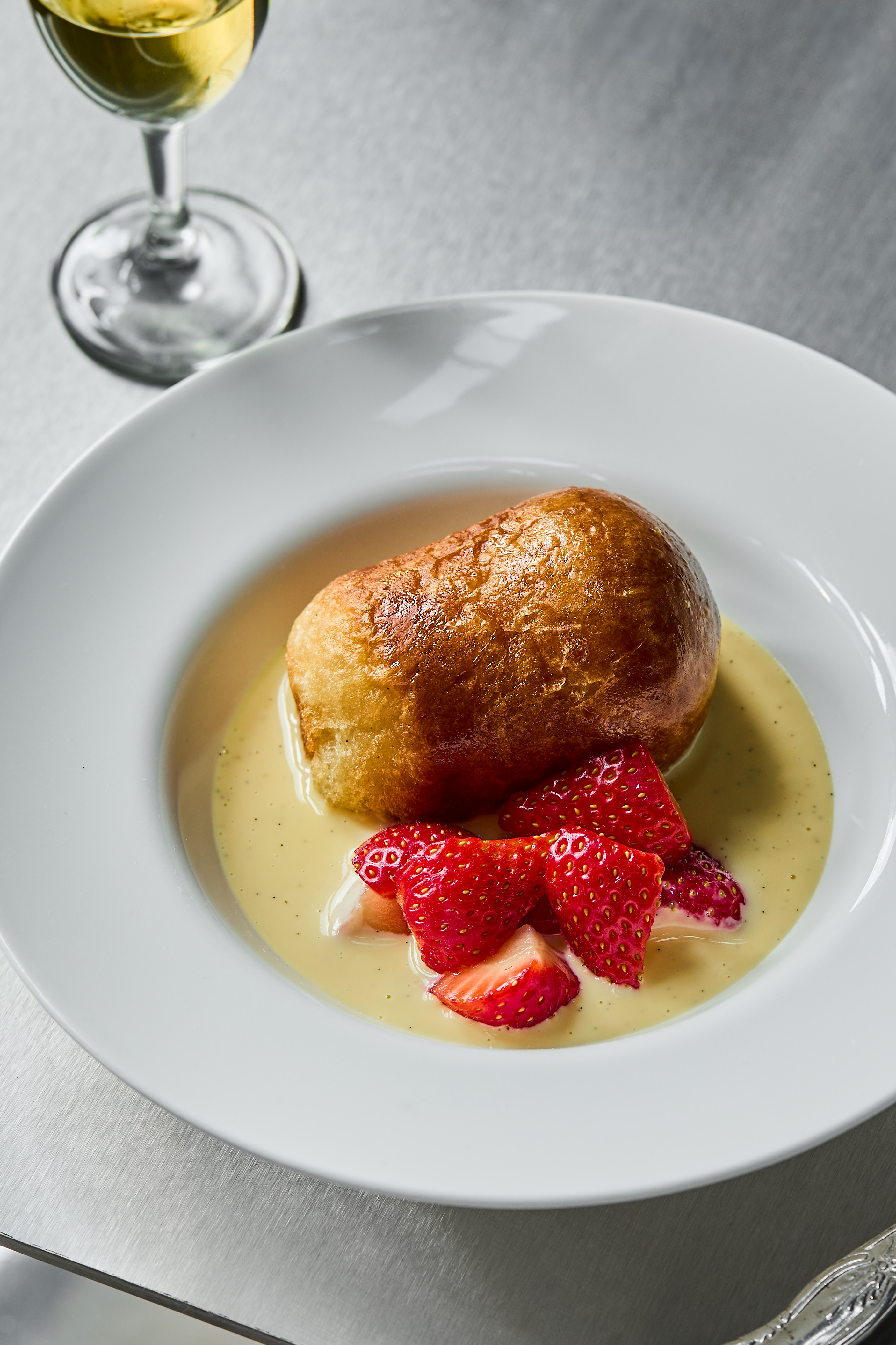 A series of beautifully presented, colorful restaurant plates and cocktails come served in white or chrome tableware and are placed atop silver tables.