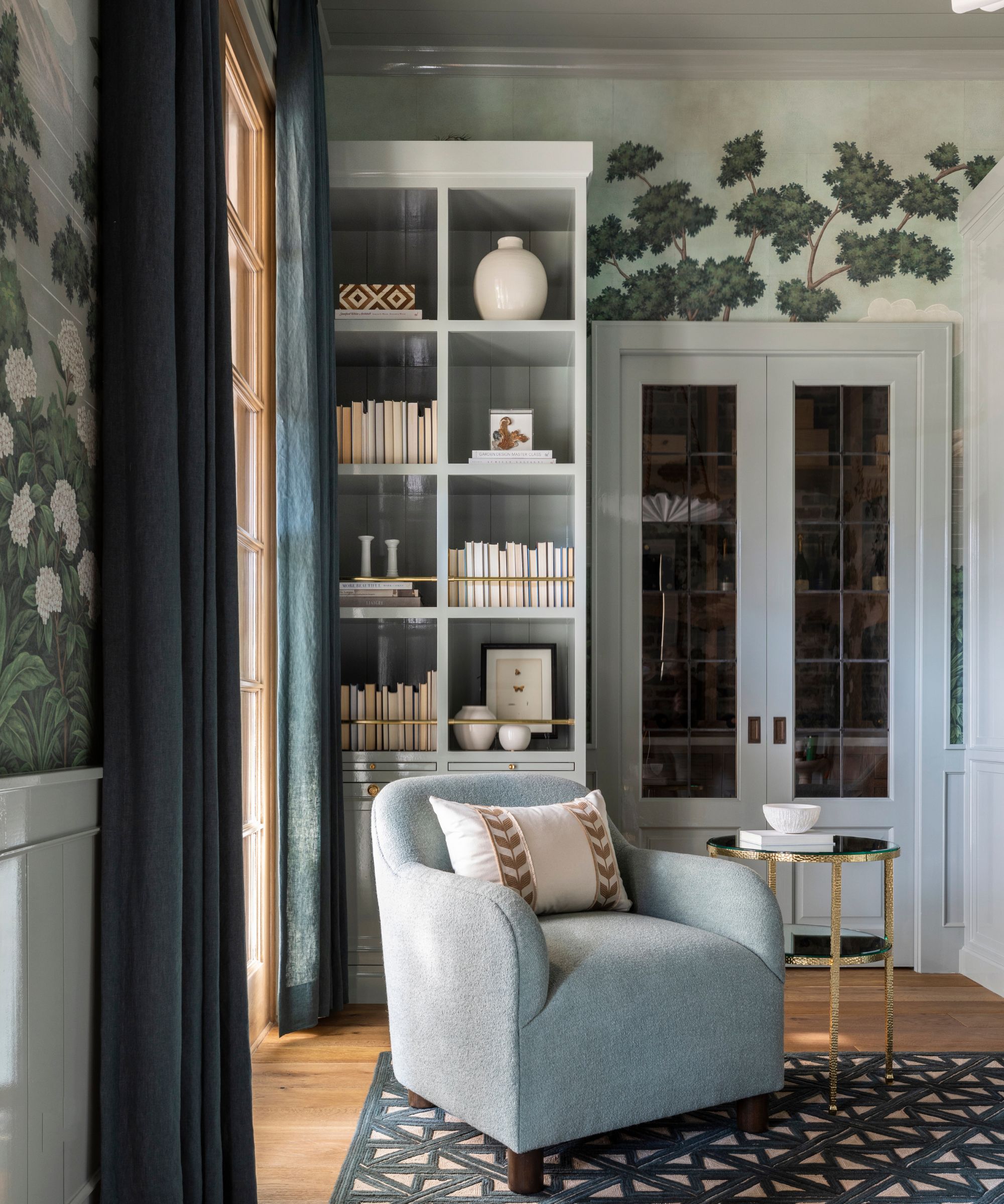 A traditional living room with pale blue decor and a forest scene wall mural.
