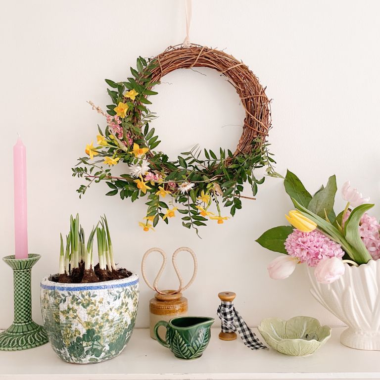 spring wreath hanging from wall with pots of spring plants, keepsakes and candles