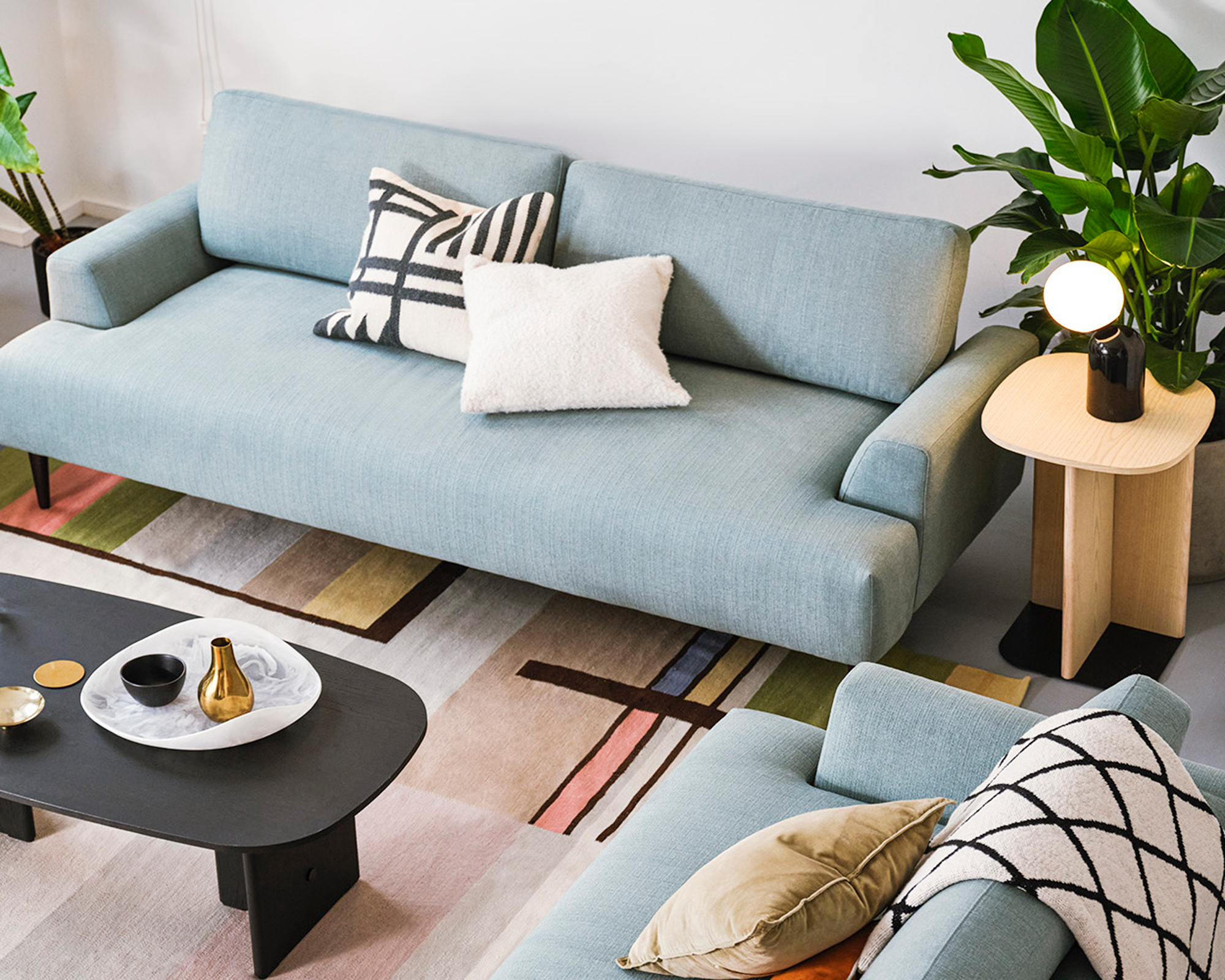 Pastel blue sofas, modern abstract rug, and graphic mono accessories, with sculptural furniture.