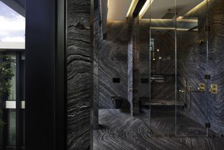 A dark grey slab shower with brass faucets and a glass seamless frame