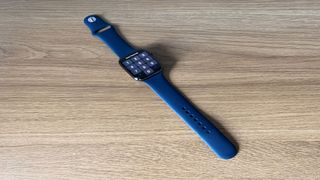 Image shows the Apple Watch Series 7 with a blue strap on a wooden table.