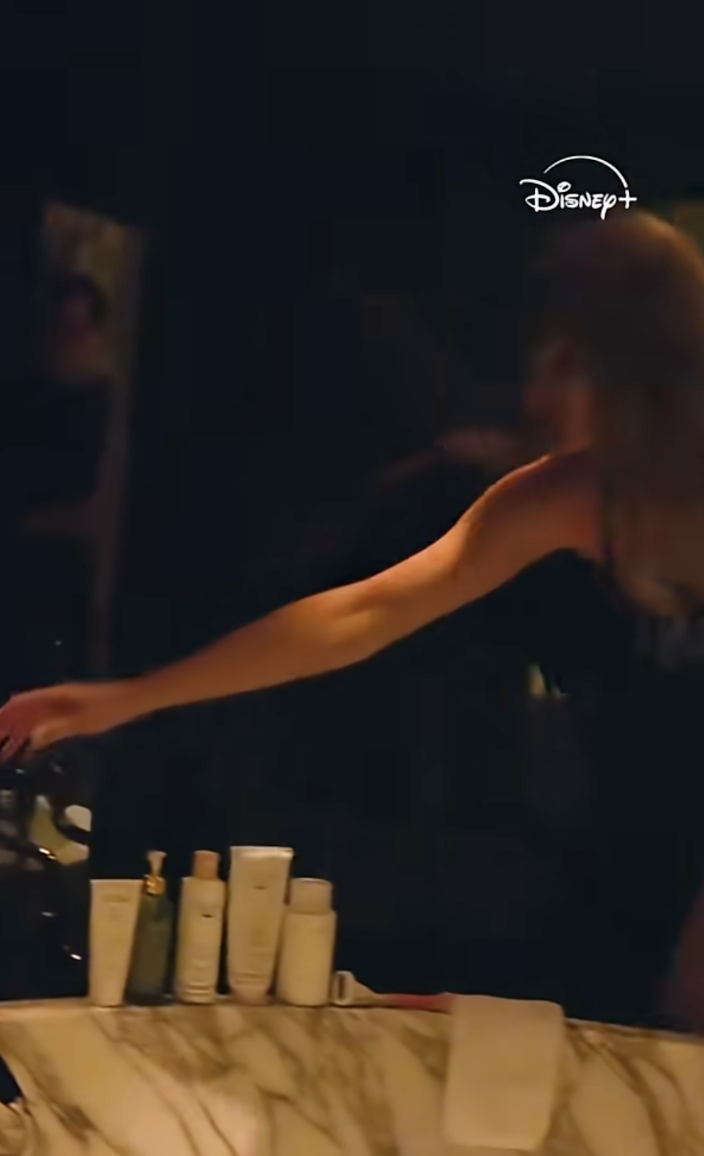 a still from a video of a woman reaching over a bathtub lined with hair and beauty products