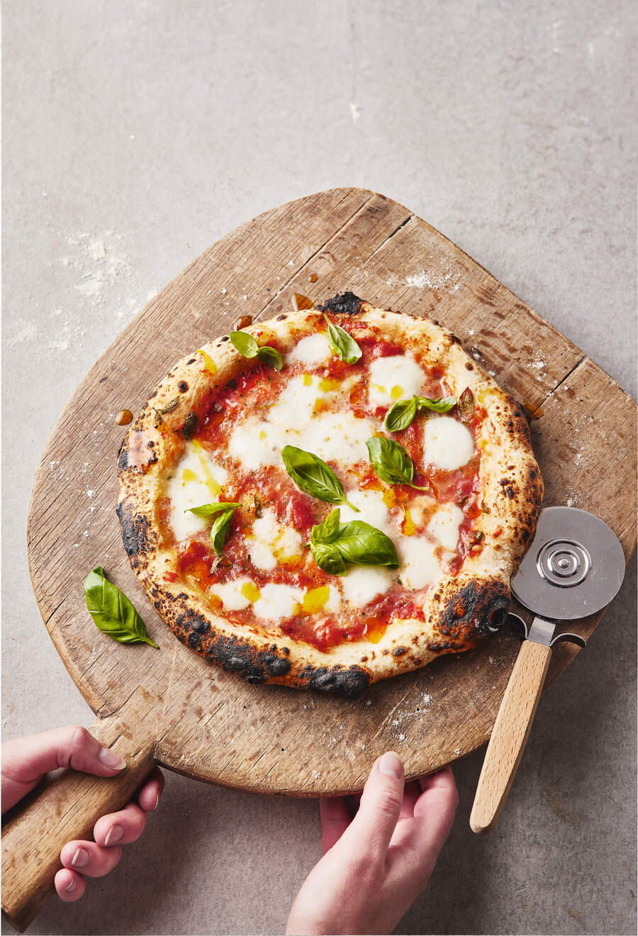 A freshly baked Neapolitan-style pizza topped with mozzarella and basil, being held on a wooden pizza peel.