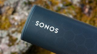 een close-up van een donkerblauwe sonos roam bluetooth-speaker met een stenen muur op de achtergrond