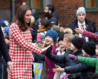 Kate Middleton in Sweden 2018 greeting children wearing her red and white houndstooth coat