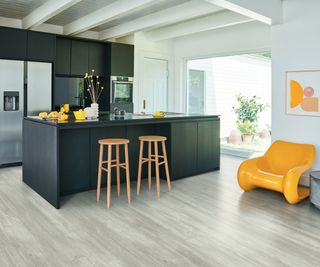 grey oak kitchen flooring in room with black kitchen cabinets and a yellow chair
