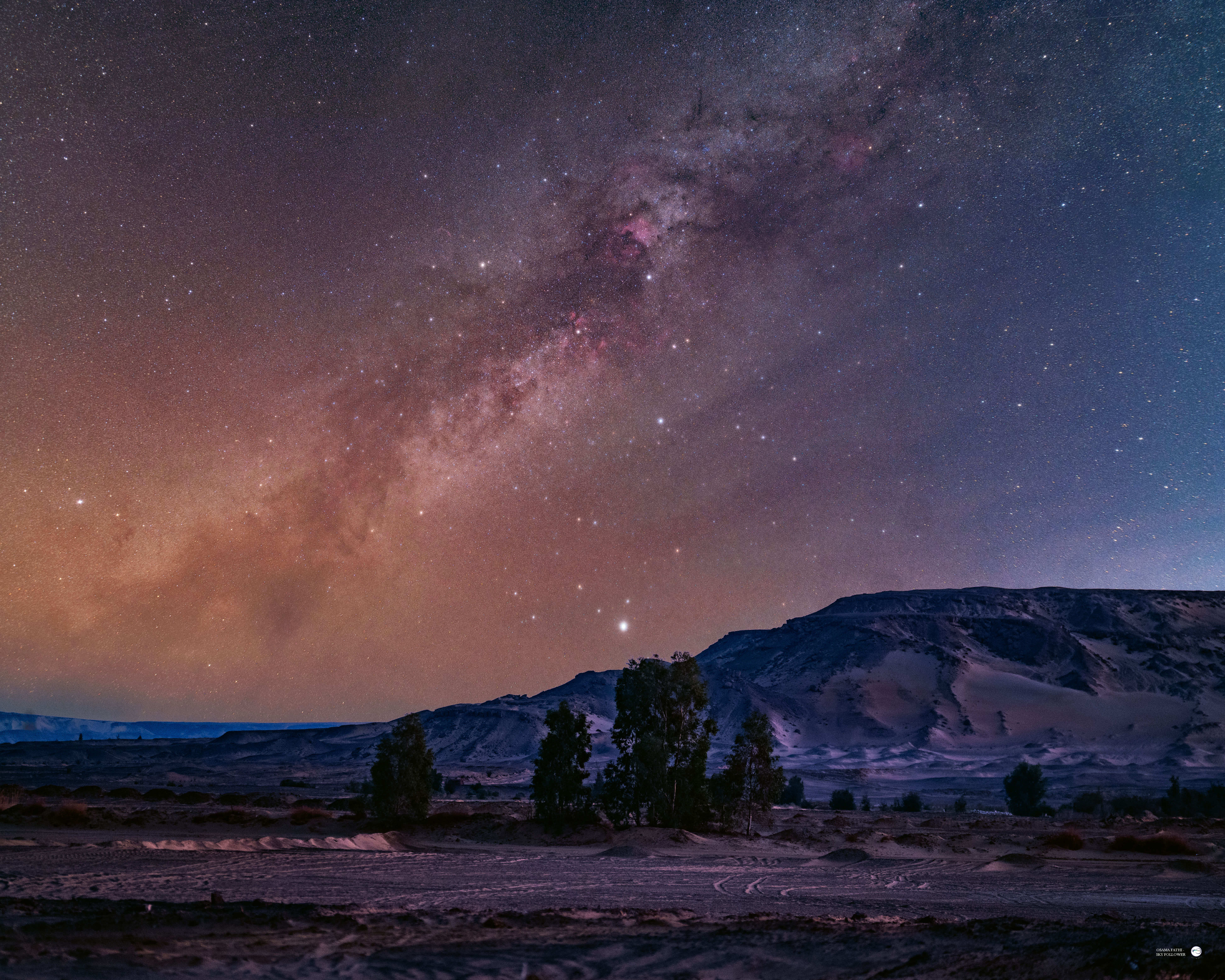 The glowing band of the Milky Way's galactic plane is pictured tumbling diagonally through a starry night sky above a mountainous region.