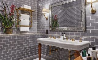 Bathroom lined with silver-grey tiles, brass fixtures and a framed mirror