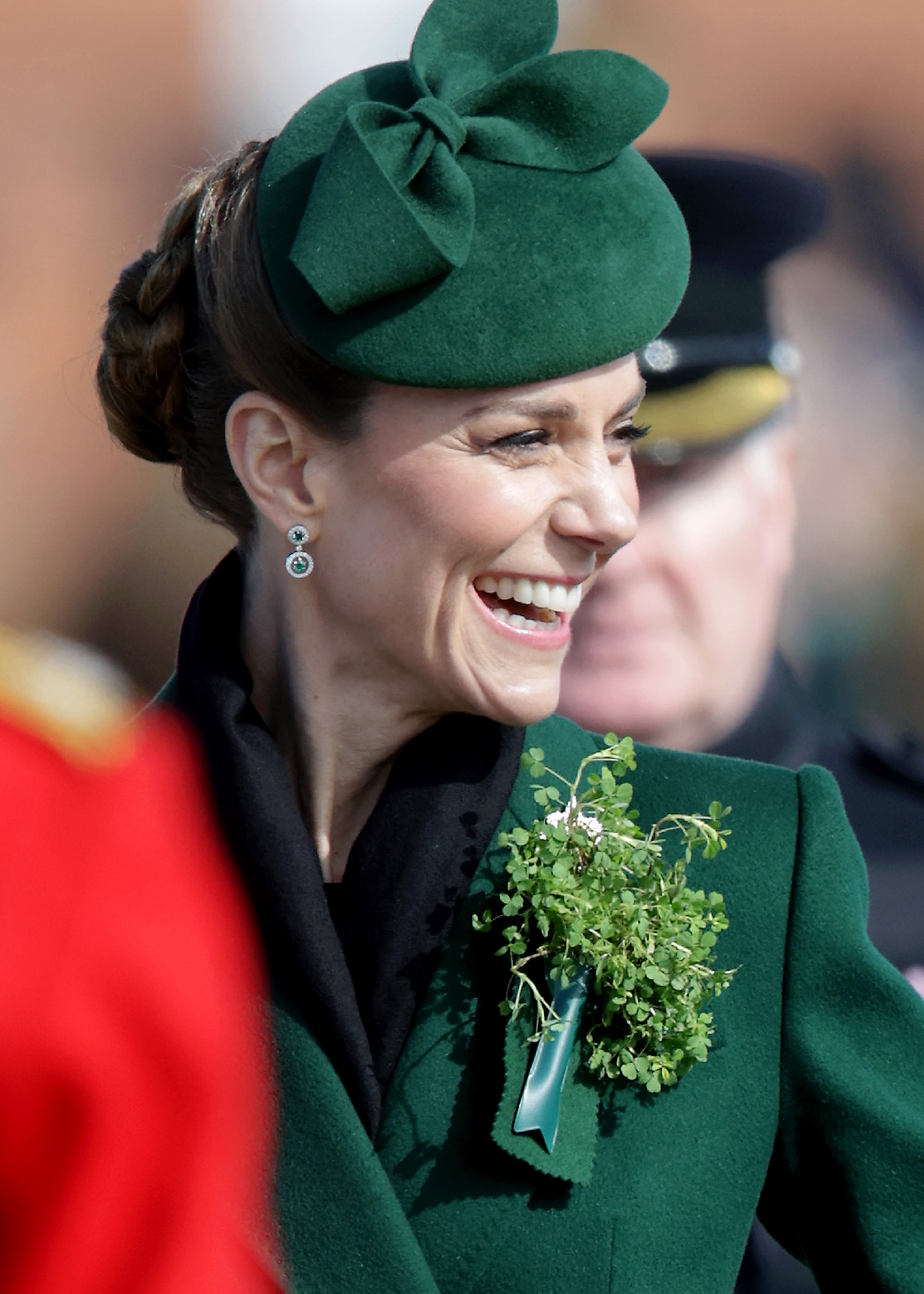 Princess Kate laughing and wearing a green coat with shamrocks pinned to it