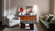 A warm, contemporary living room with an olive green sofa, sculptural cream armchair, wooden sideboard, statement art and a coffee table.