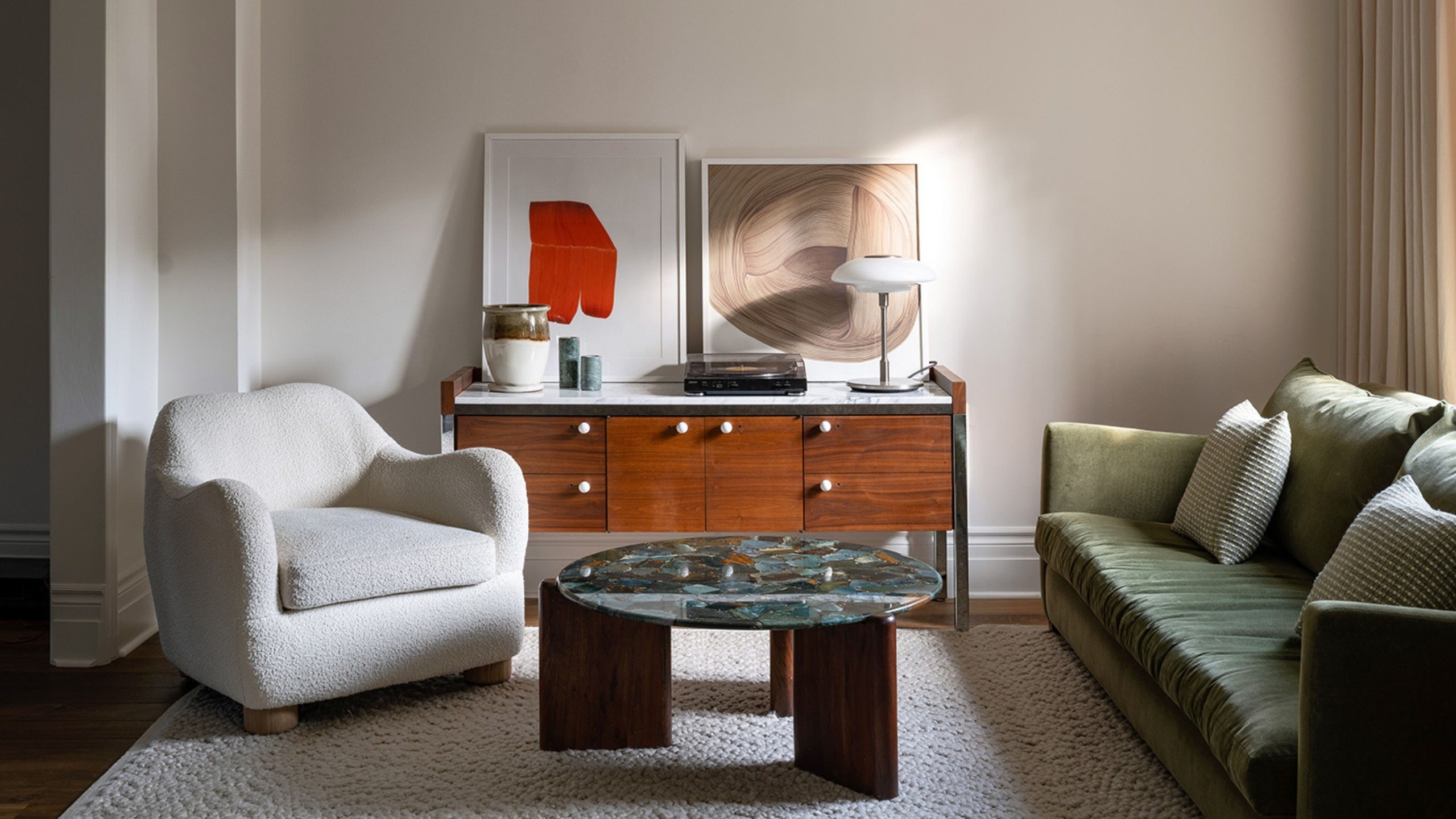 A warm, contemporary living room with an olive green sofa, sculptural cream armchair, wooden sideboard, statement art and a coffee table.