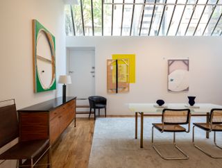 Interior of 30 Bond Street apartment with contemporary furniture featuring a wood side board, a glass table and two chairs in the centre of the room, three pieces of artwork on display on the walls. The ceiling is clear glass
