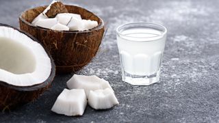 Small glass of coconut water, one of the alternatives to alcohol, sitting on stone worksurface with coconuts