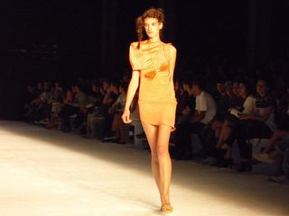 Model on a runway wearing a peach-coloured dress with silk detailing