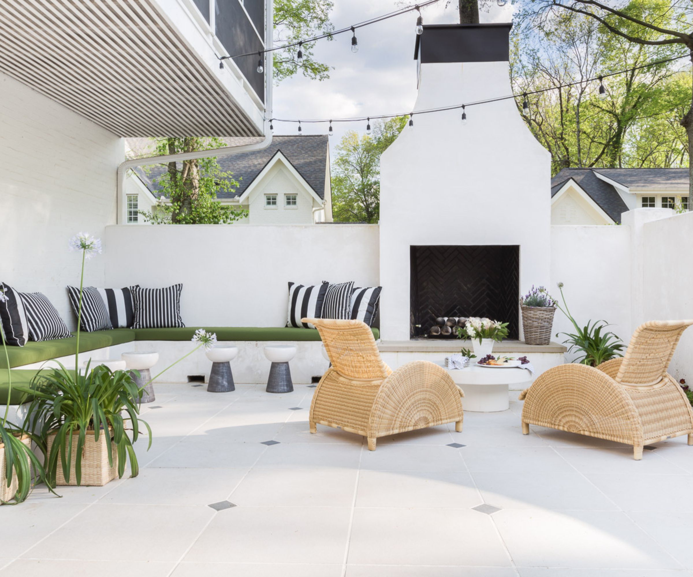 Outdoor courtyard with white tiles and white painted walls and outdoor fireplace, built-in seating and two rattan loungers