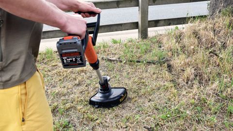 Black + Decker LSTE525 Cordless Lawn Trimmer in use on patch of grass near road