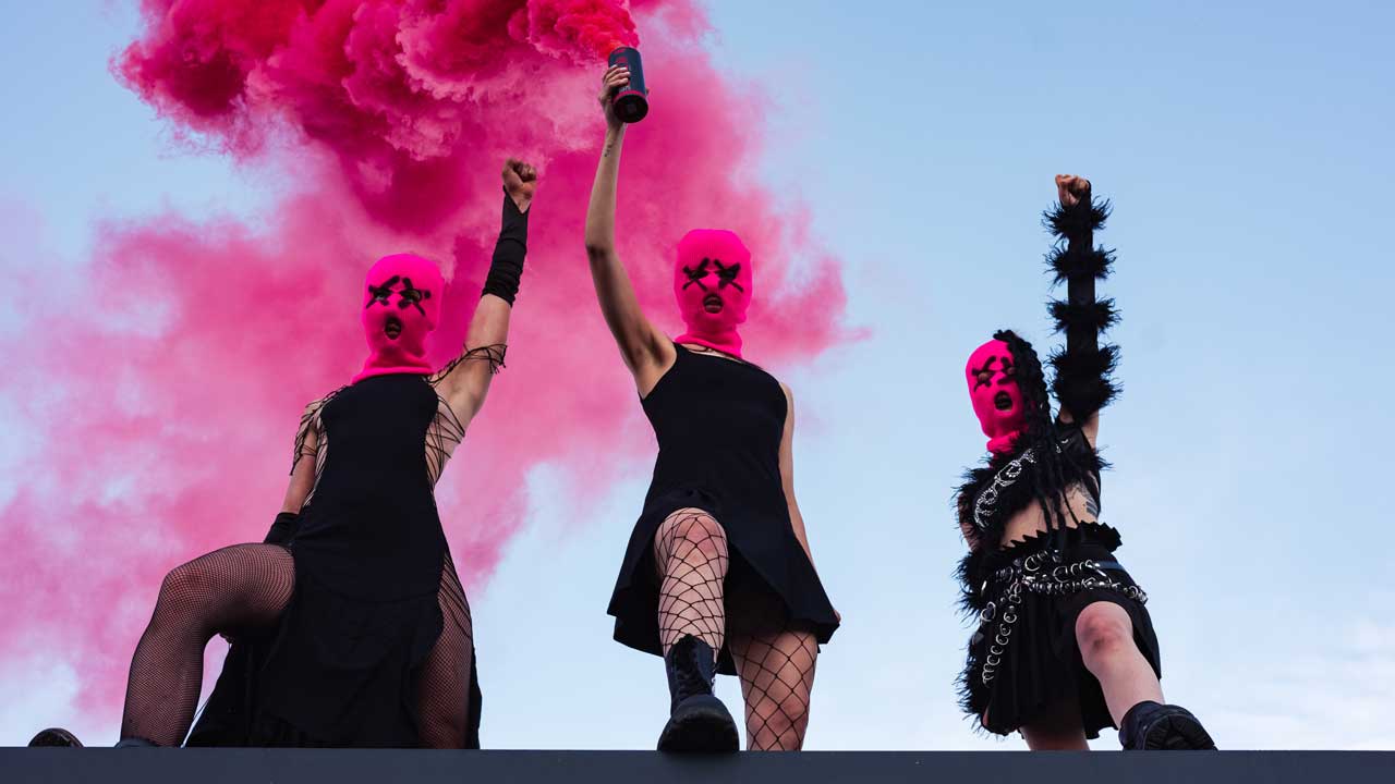 Pussy Riot on a rooftop holding a pink smoke flare