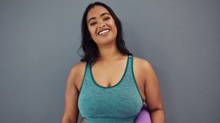 Woman in sports bra holding yoga mat and smiling