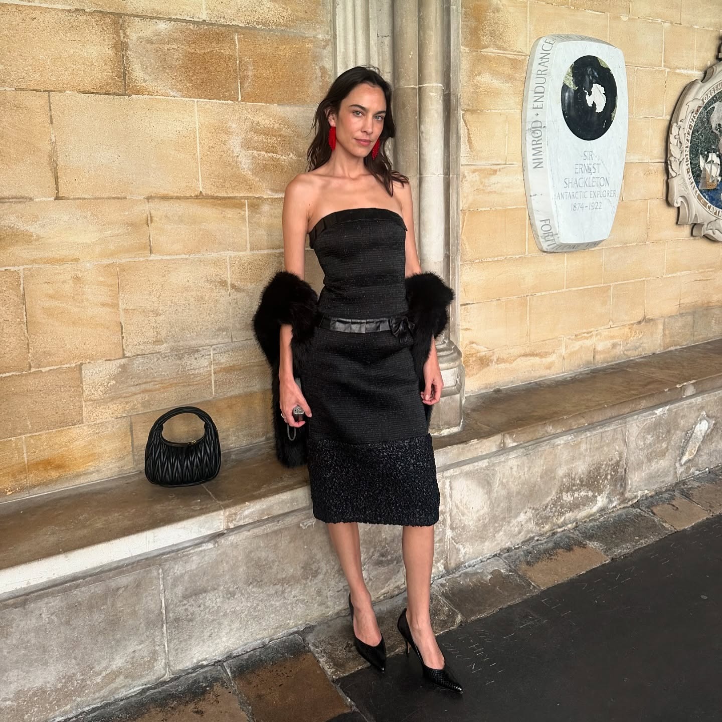 Alexa Chung wears a strapless black dress with mid-heel pumps and red earrings.