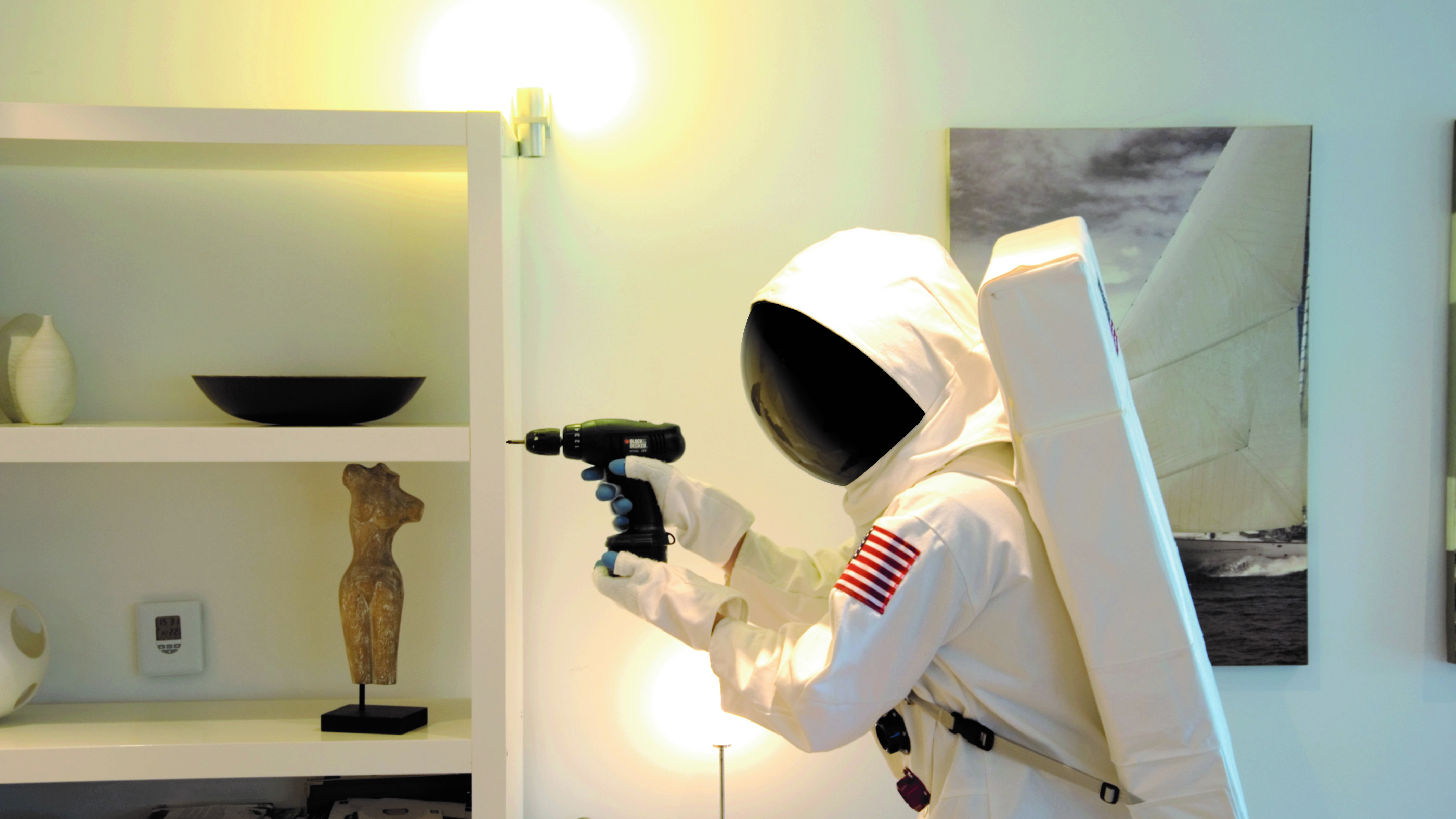 A person in an astronaut costume uses a cordless drill at home.
