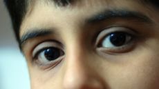 A close up of a boy's face, his dark eyes look into the camera