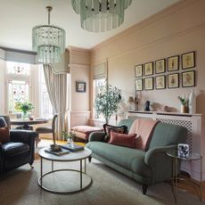 sitting room with blush pink walls, green sofa and armchair, with round coffee table and gallery of prints on wall.