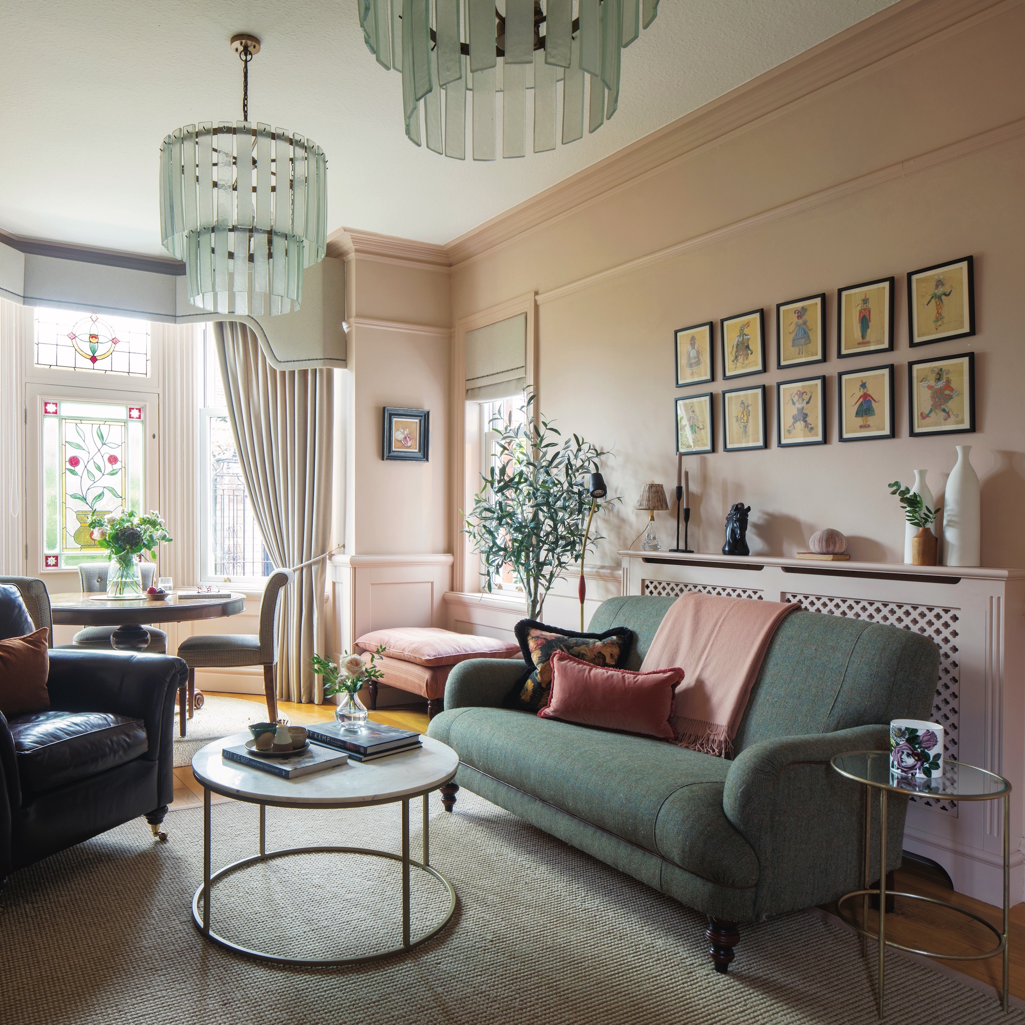 sitting room with blush pink walls, green sofa and armchair, with round coffee table and gallery of prints on wall.