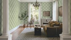 Cozy small living room with hard floors and radiator in view. There is a sofa, ottoman coffee table, and patterned sage wallpaper