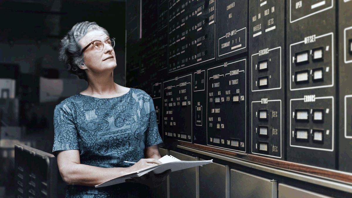 a woman in glasses carries a notebook and pencil beside a wall covered in instrument panels and lights