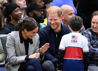 Prince Harry and Meghan Markle laughing as they talk to a young boy in the audience wearing a Team USA family shirt at an Invictus Games event