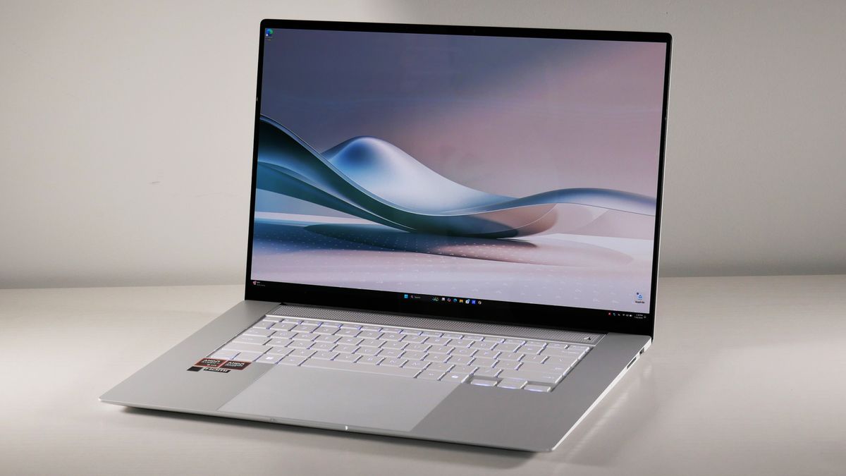 An open and powered-on light-colored laptop on a white desktop against a white wall.