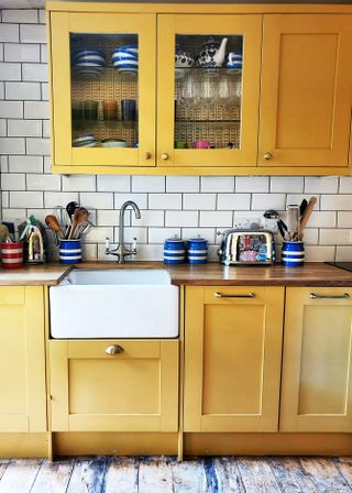 yellow kitchen cabinets with deep white sink and striped storage jars white tiles and bare floorboards
