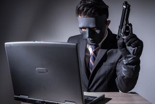 Abstract image of hacker or criminal wearing a mask and suit, using a laptop and holding a gun.