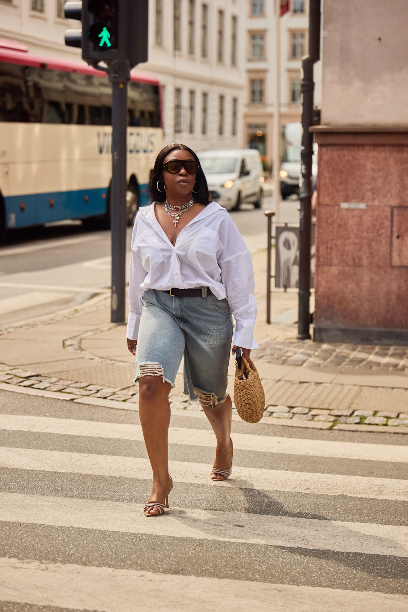 woman wearing ripped jean shorts, a button-down top, sandals, and a bag