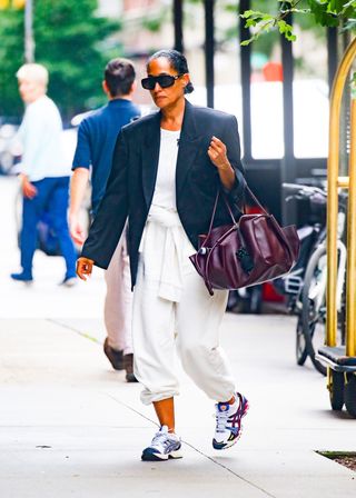 Tracee Ellis Ross carries a burgundy bag with a black blazer, a white t-shirt, white sweatpants, and multicolored Asics sneakers.