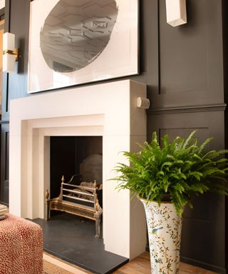 A black living room with a white fireplace, white wall art, and a vase with a plant next to it