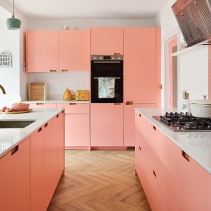 pink kitchen cabinets with a pink kitchen island and herringbone wood flooring